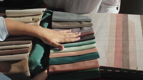 a woman's hand strokes the fabric samples that the designer holds next to the wallpaper samples. selection of finishing materials for home repair