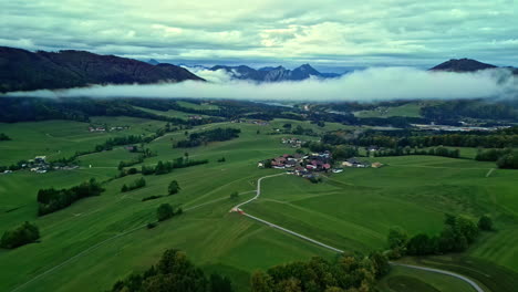 Bus-driving-to-alpine-mountain-valley-village,-cloud-hovering-over-it