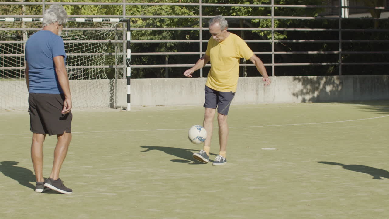 deportistas senior atléticos practicando habilidades con pelota de fútbol en el campo