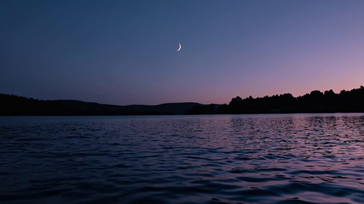 Scène sereine d’un lac au crépuscule avec un croissant de lune, capturée depuis un angle bas