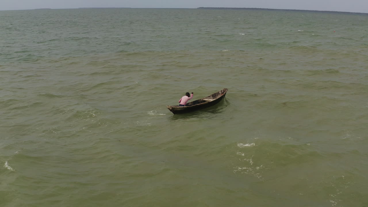 un hombre remando en una canoa de madera contra las olas y el viento en un día soleado, cerca de la costa de dar es salaam, tanzania