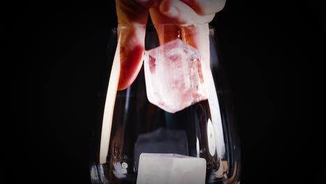 la mano deja caer un cubo de hielo en un vaso vacío