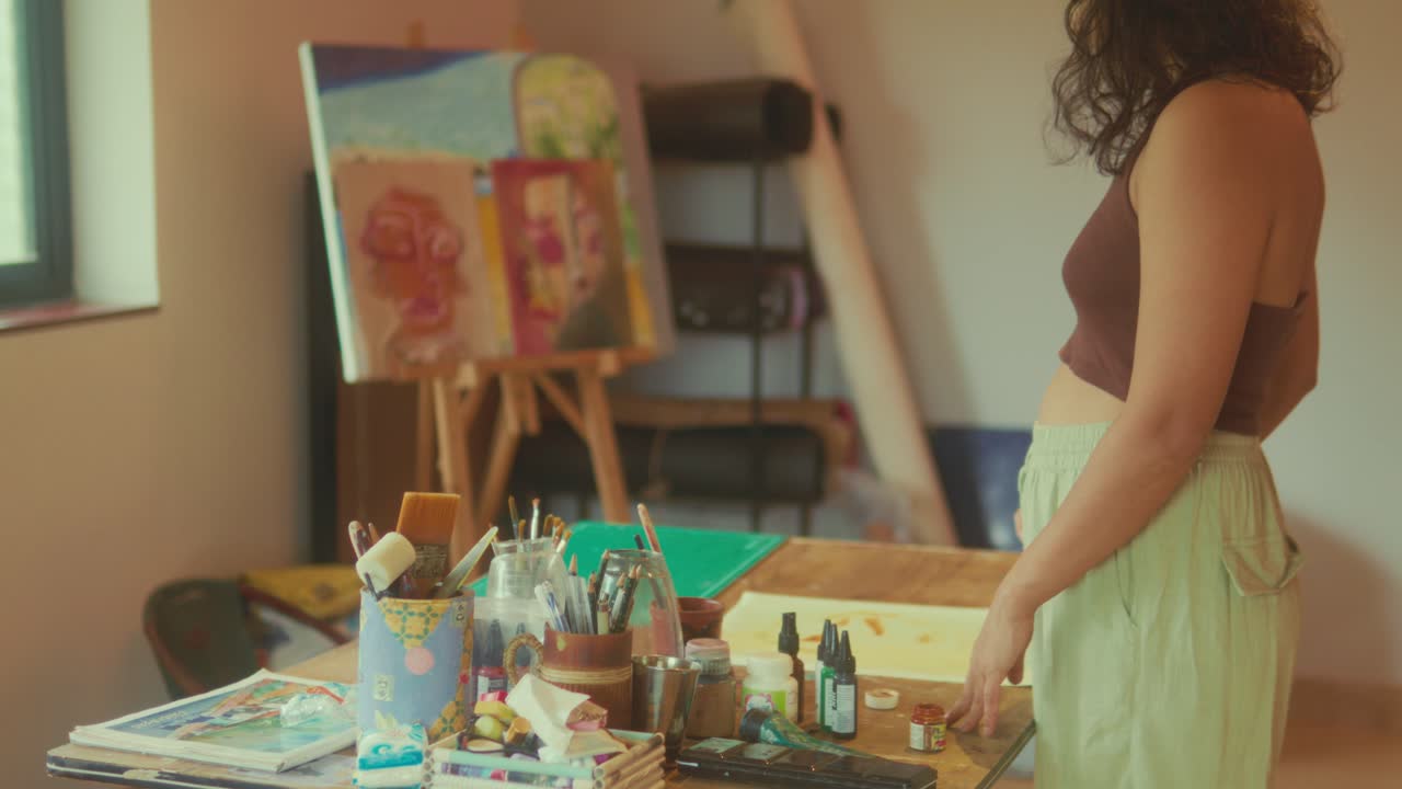 Donna in piedi vicino a un tavolo con strumenti artistici e una tela in uno studio creativo, scena di vita al chiuso