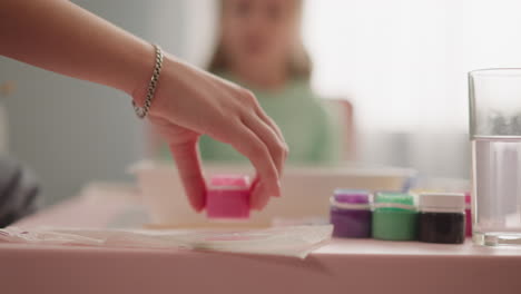 teacher hand takes bottle with pink paint girl sits at table