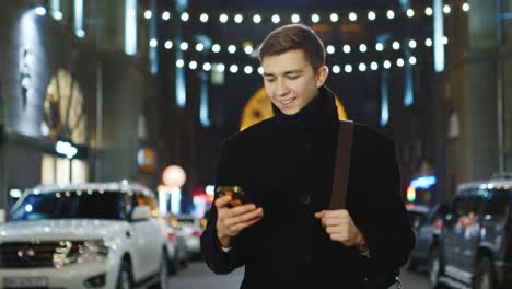 un joven camina por la ciudad nocturna y usa un teléfono inteligente 3