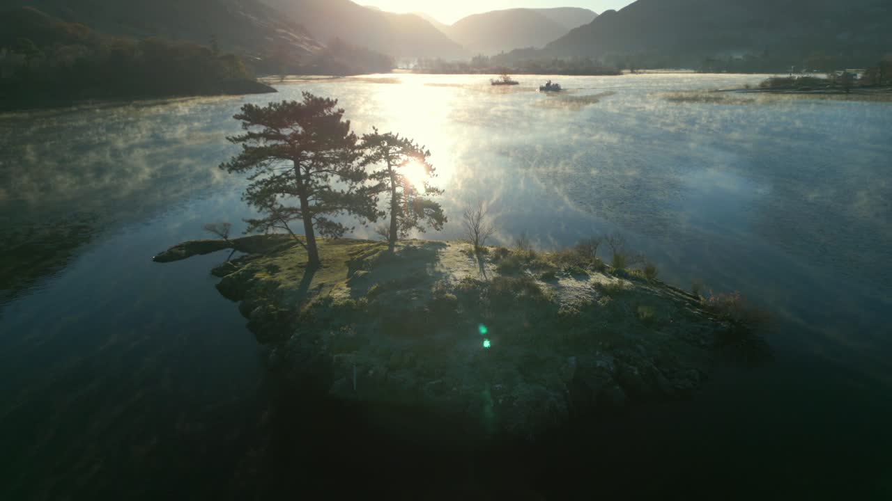 평온한 안개 호수에 있는 작은 섬에서 해가 뜨는 모습이 물에 반사되어 카메라가 아오르면서 해가 나고 산맥의 실루이 드러납니다.
