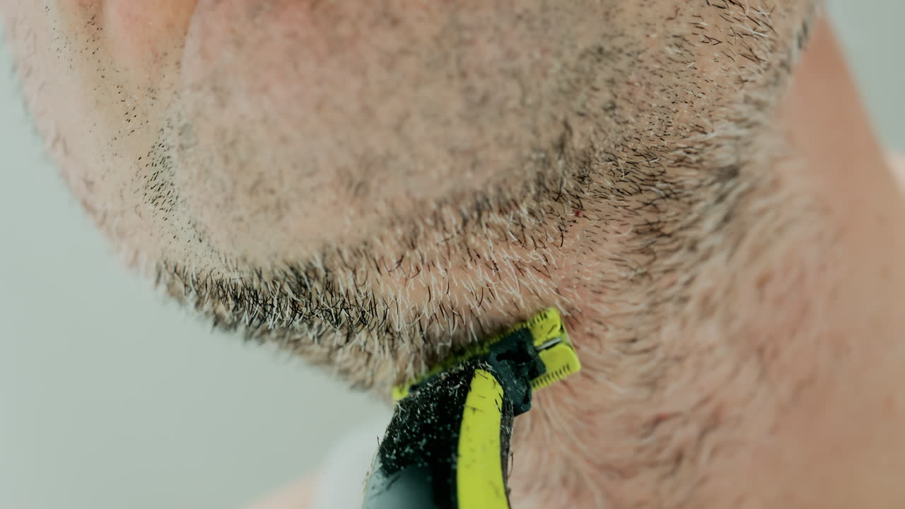 Close up of a man using an electric razor to trim facial hair in the bathroom