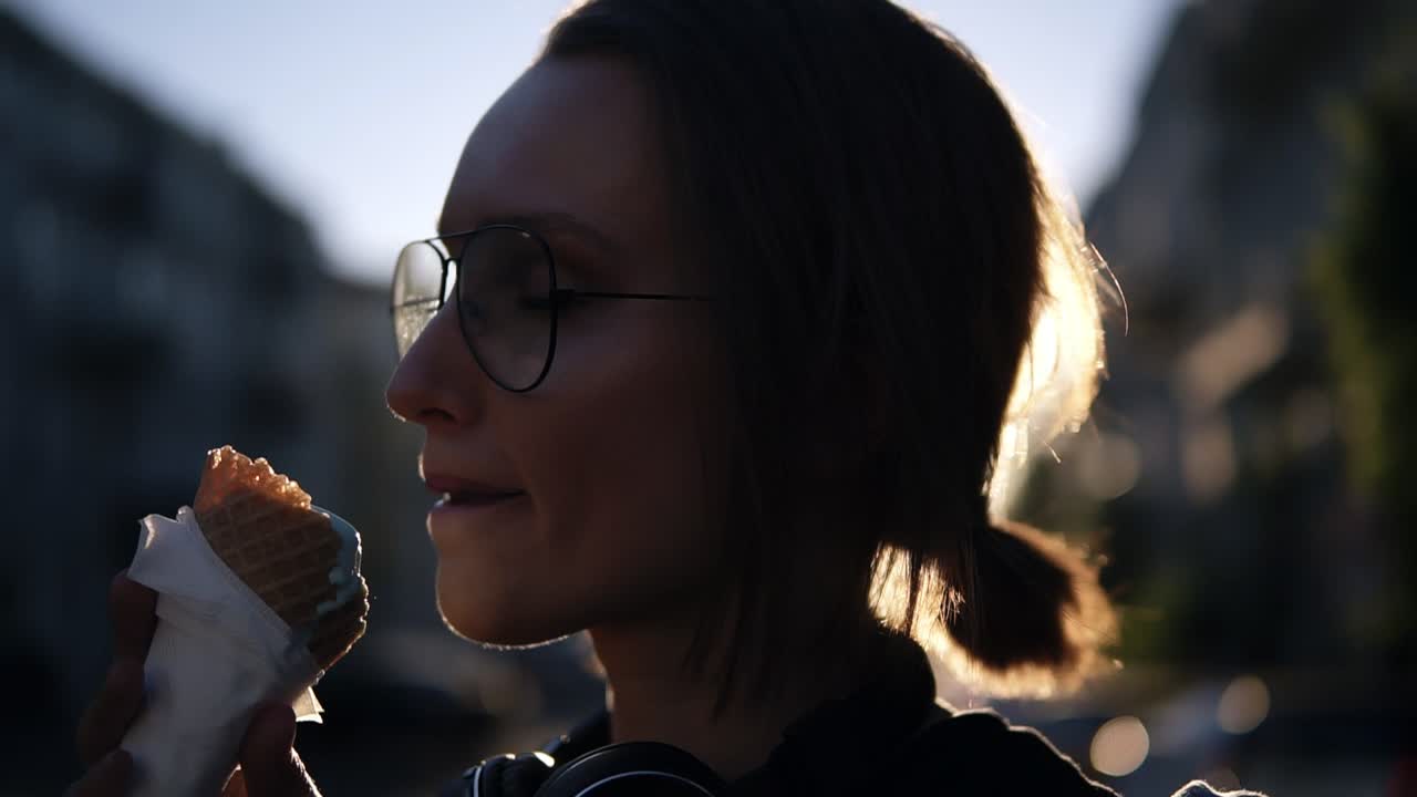 Portrait of a young blonde girl licking and ice-cream in waffle cone on the street. son shines on the background. Delicious