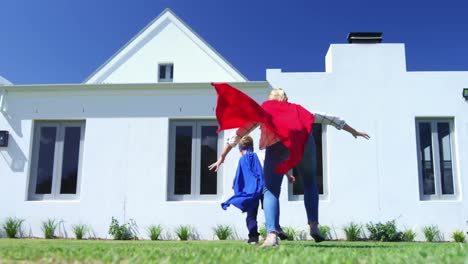 Wow-Text-Auf-Sprechblase-Gegen-Mutter-Und-Sohn-Im-Superheldenkostüm,-Die-Im-Garten-Laufen