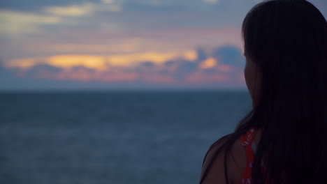 vista trasera de una mujer coreana observando una impresionante puesta de sol con un cielo nublado y dramático junto al océano, retrato con espacio para copiar