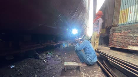 dock worker using welding torch on ships hull at shipyard in bangladesh