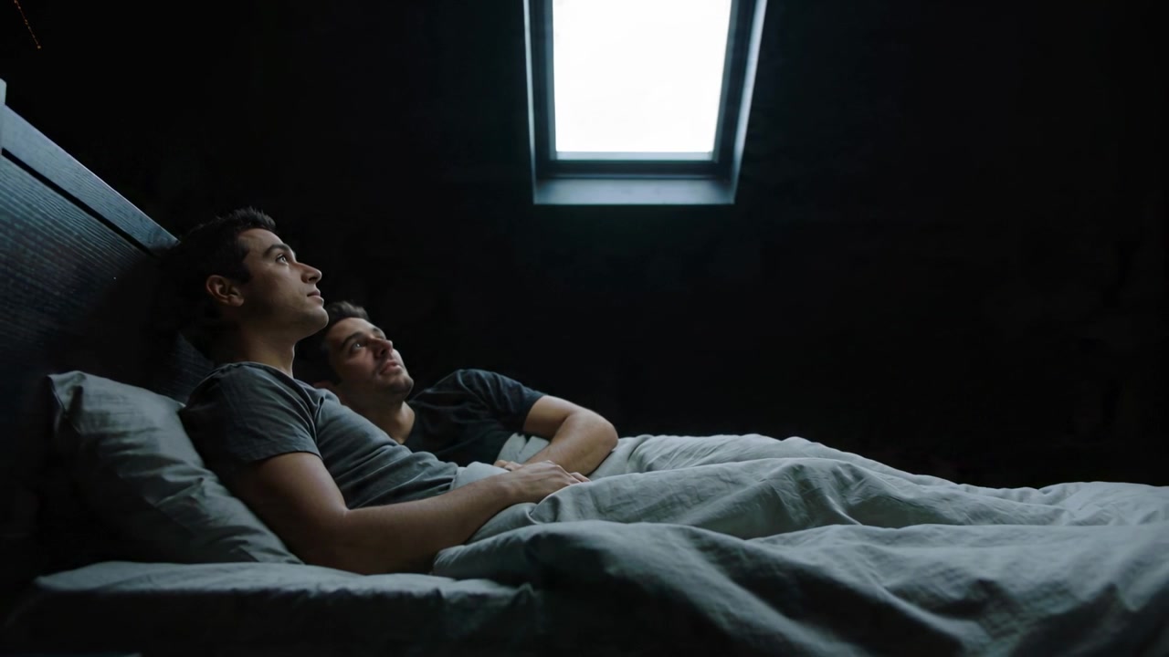 Attirant le regard, puits de lumière lumineux attirant un couple d'hommes en manches courtes sur un lit, l'un posant sa tête.
