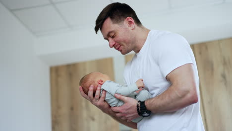 loving smiling man rocking a tiny baby. new made father takes care of his child in maternity hospital. low angle view.