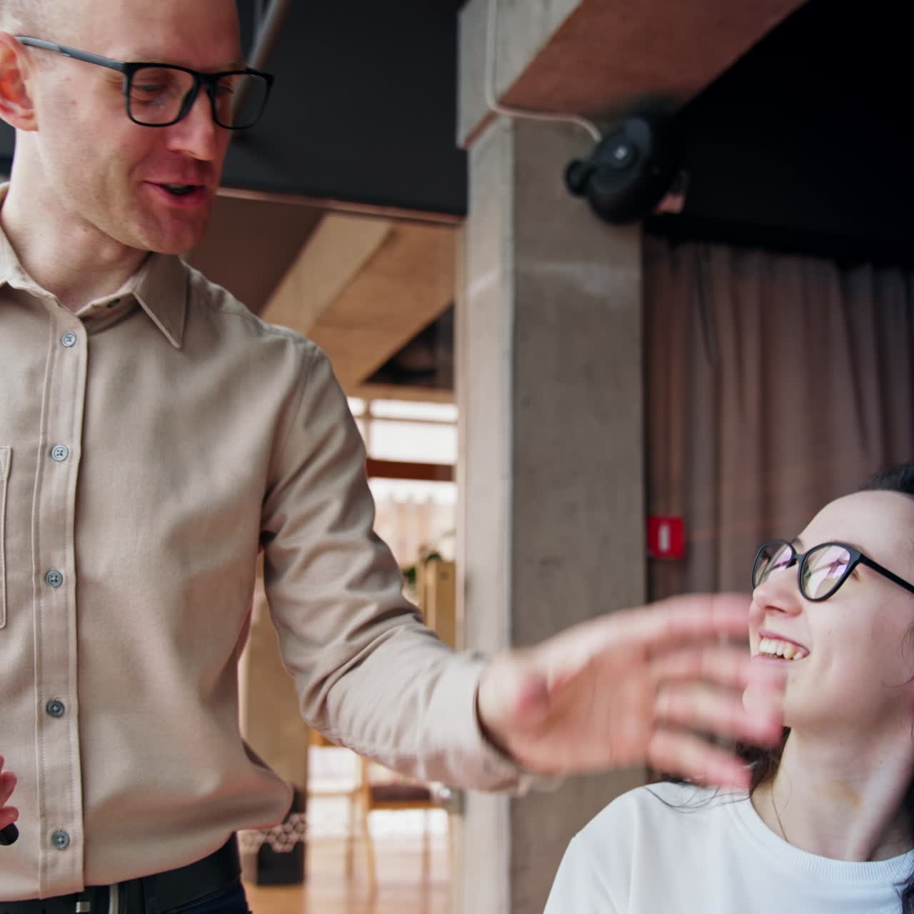 Brunette woman shows paper notebook to a male colleague. Male co-worker points at notebook with his finger and both laugh