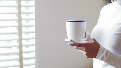 woman using mobile phone while having cup of coffee