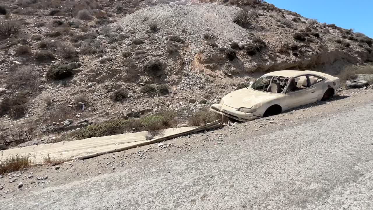 Remote road along Cedros Island’s arid landscape with rugged terrain and sparse vegetation and broken looted cars
