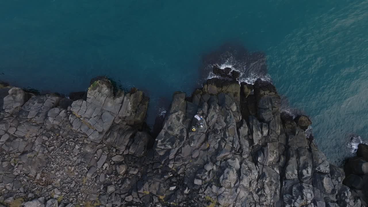 Fisherman's on basaltic rocks, waves splashing into volcanic cliff - aerial 4k