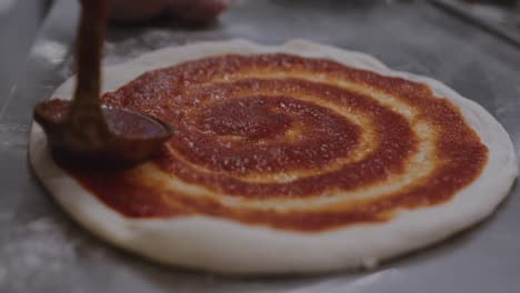 smearing tomato sauce on top of formed pizza dough