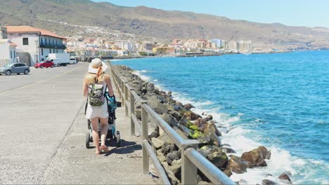 young mother with baby stroller walking on candelaria township coastline