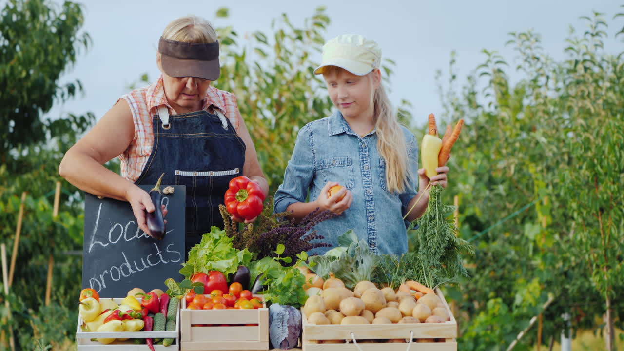 할머니와 손녀는 농민 시장의 카운터에 야채를 낳는다