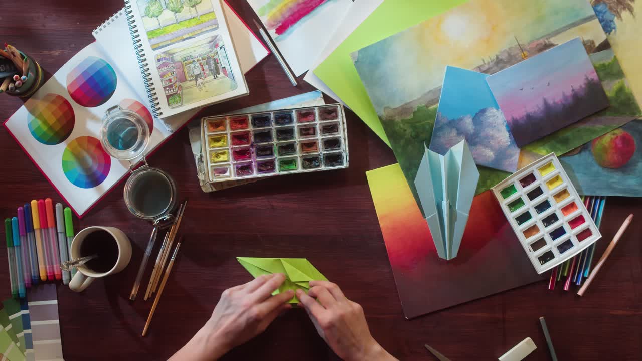 Vista dall'alto di mani che piegano carta origami verde su una scrivania da disegno.