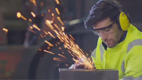 caucasian male worker in a safty uniform wear welders leathers,electric wheel grinding on steel structure in factor in the garage, orange bokeh sparks fly to the sides