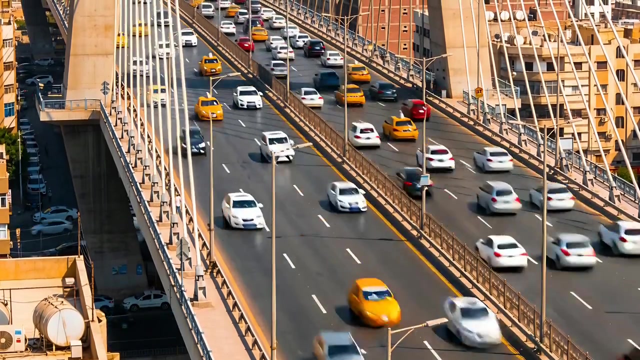 Mostra traffico su più corsie che si muove su un ponte strallato in un'area urbana, con taxi gialli e pedoni.