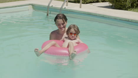 cheerful little boy floating on inflatable ring in swimming pool with the help of his brother