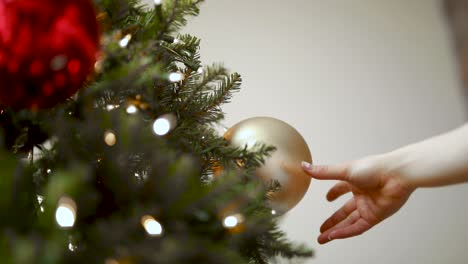 Frauenhand-Hängt-Eine-Goldene-Weihnachtskugel-Am-Weihnachtsbaum---Weihnachtsferienzeit