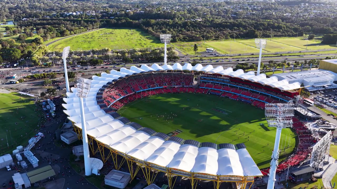 High-angle drone shot pans across a large outdoor stadium during daylight in a suburb.