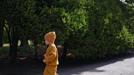 baby boy wearing yellow cap and clothes runs by the path and stops noticing something interesting. sunny day walk in nature.