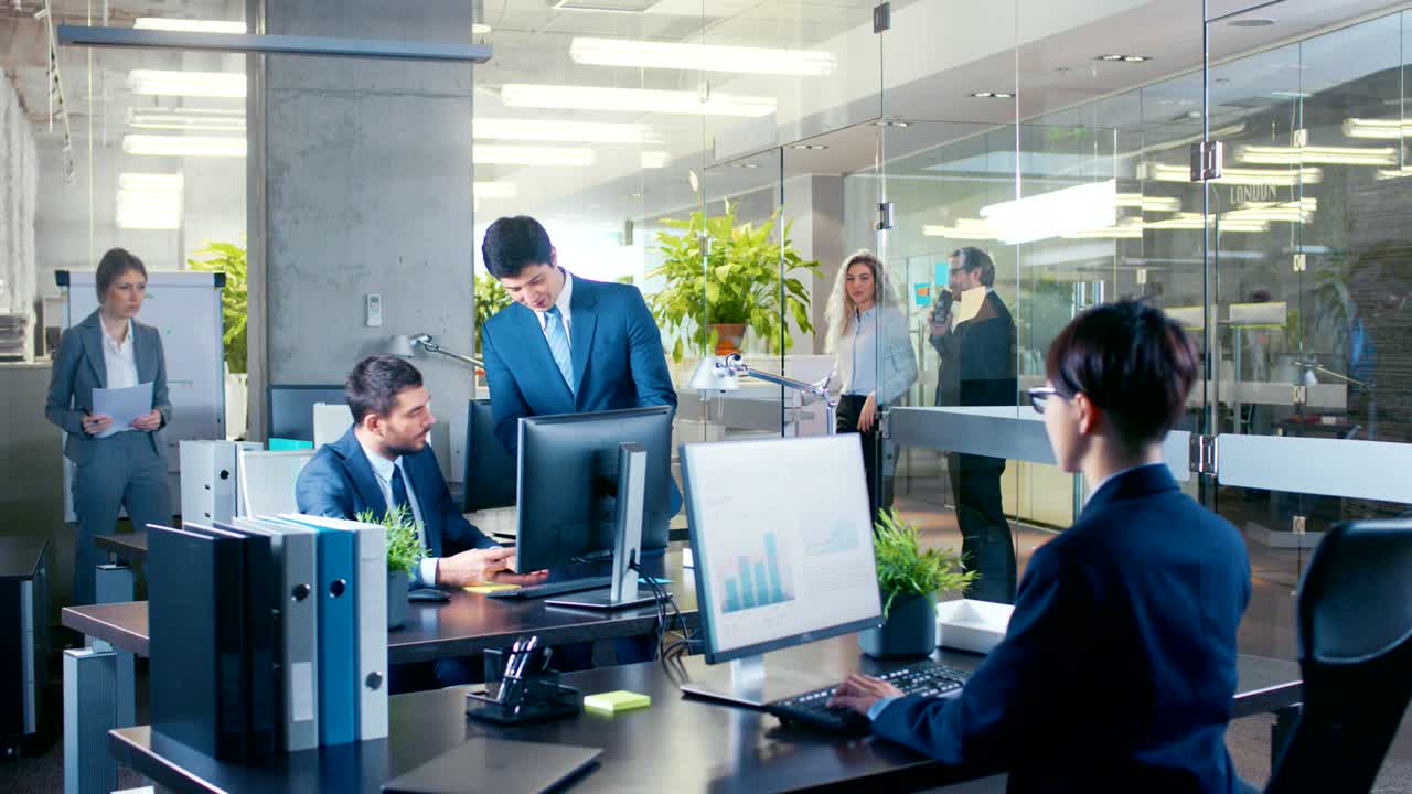 파노라마 은 직원이 매니저에게 중요한 소식을 전하고, 정보가 담긴 태블릿 컴퓨터를 보여주는 사무실입니다. 현대적인 유리와 콘크리트 건물은 바쁜 사업가들로 가득 차 있습니다.