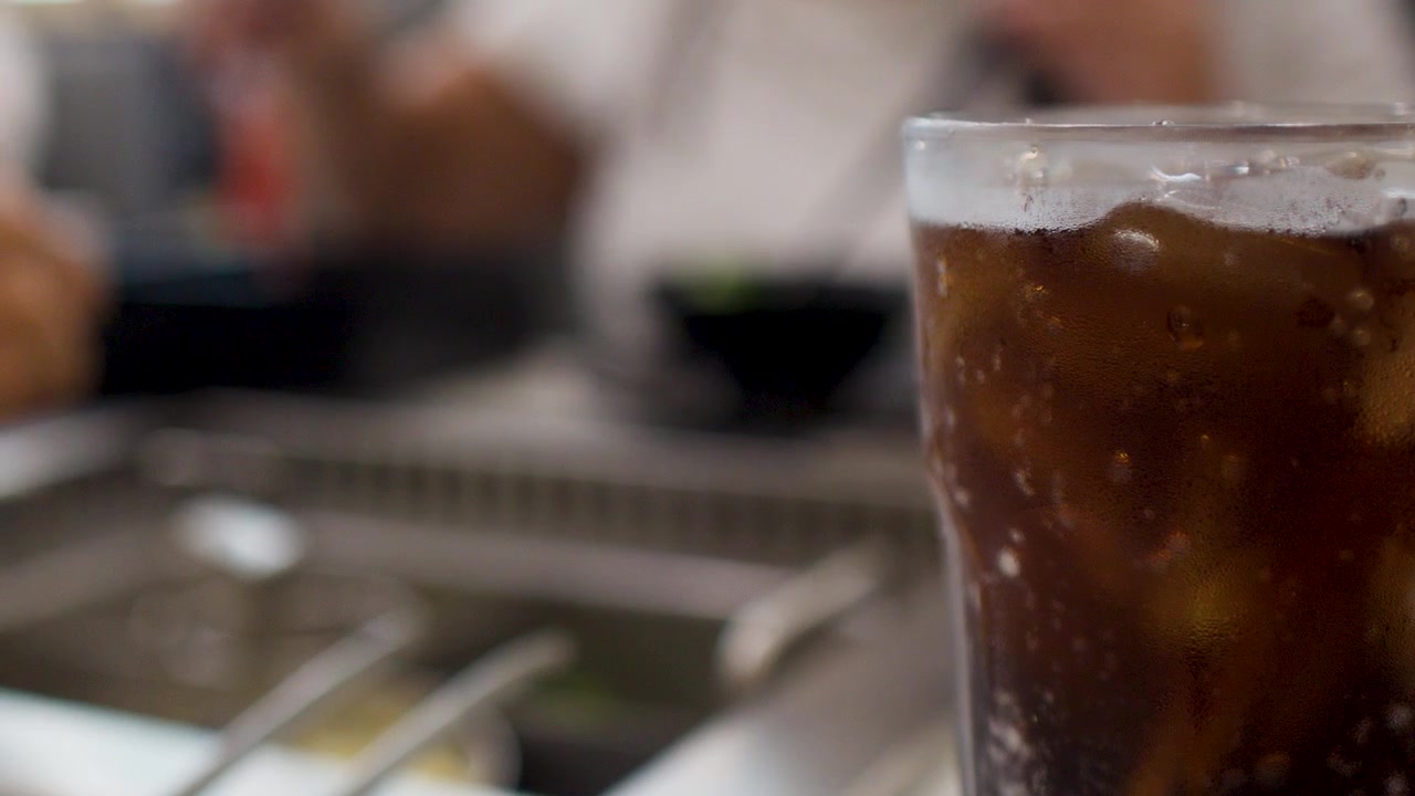Primo piano di una bibita cola frizzante con ghiaccio su un tavolo durante un pranzo sociale.