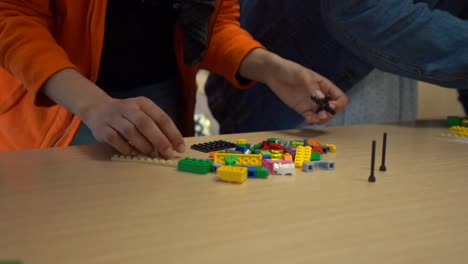 colorful interlocking plastic brick pile in front of young caucasian hand picking up black piece, close up slow motion