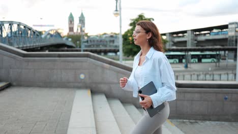 modern young businesswoman with tablet purposefully walking up steps against urban background, concept career advancement female empowerment