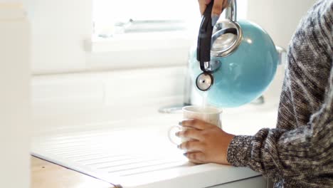 vrouw die warm water uit een ketel in een beker in de keuken giet