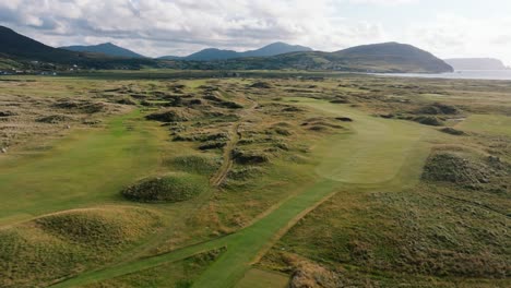 stunning ireland golf course, green fairways along coastline with mountains in background, drone, aerial