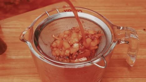 pouring fruit mix out of sous vide plastic bag into glass bowl through the fine strainer