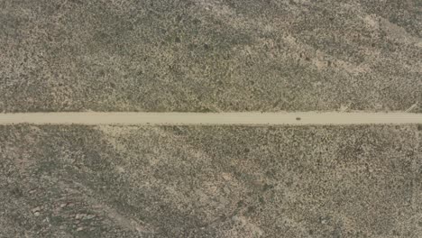 drone vuela muy alto en la vista de pájaro sobre una carretera donde un vehículo fuera de carretera negro está conduciendo en el área silvestre de cederberg en sudáfrica