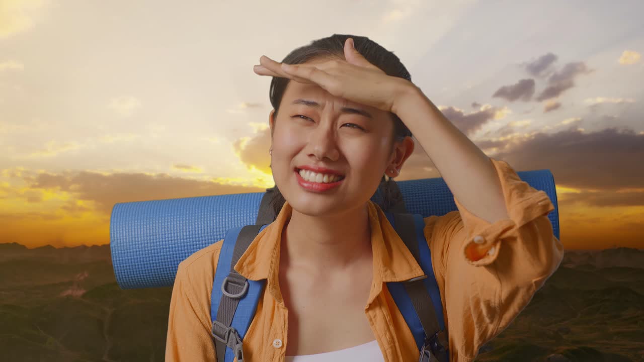 Close Up Of Asian Female Hiker With Mountaineering Backpack Hand Forehead Smiling And Looking Distance While Standing On The Top Of Mountain During Sunset Time