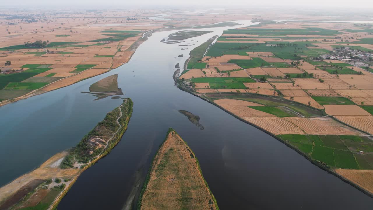 Aerial view of a river dividing expansive patchwork farmland in Punjab, Pakistan