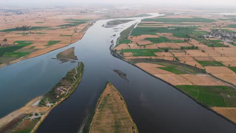 aerial view of a river dividing expansive patchwork farmland in punjab, pakistan