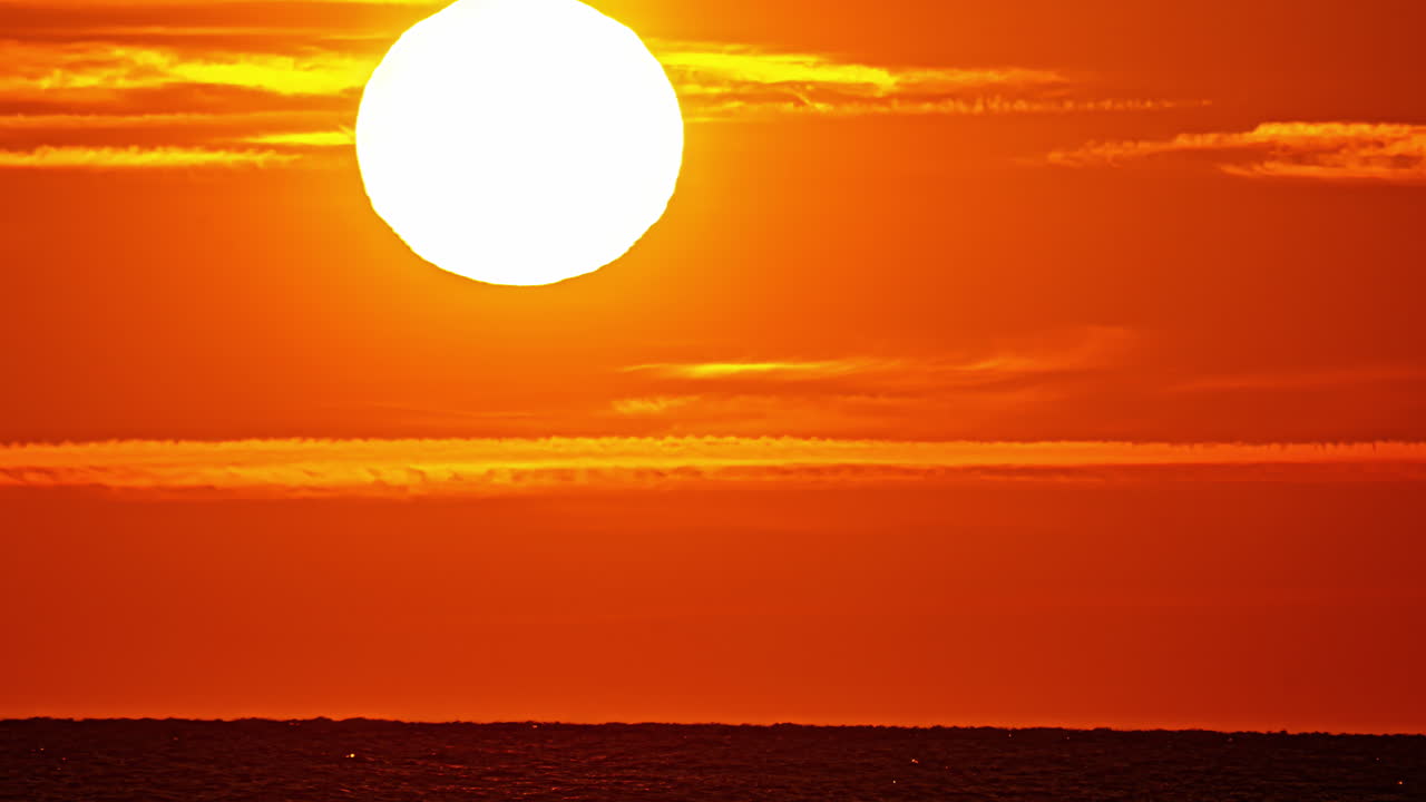 Beautiful fully orange landscape with the sun setting on the horizon over the sea at sunset with a telephoto lens
