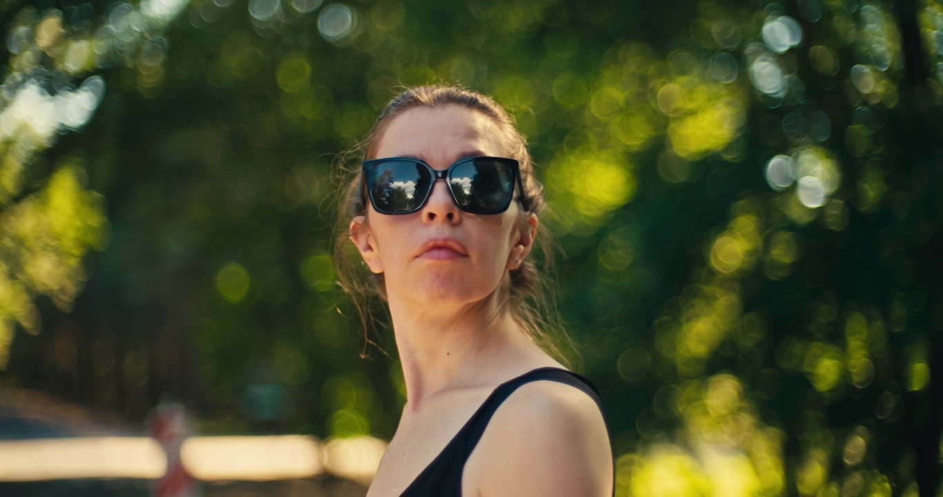 Portret in zijprofiel van een vrouw met zonnebril in een zonovergoten bos. Warm natuurlijk licht en een zacht vervaagde bosachtergrond creëren een ontspannen buitenleven scène.