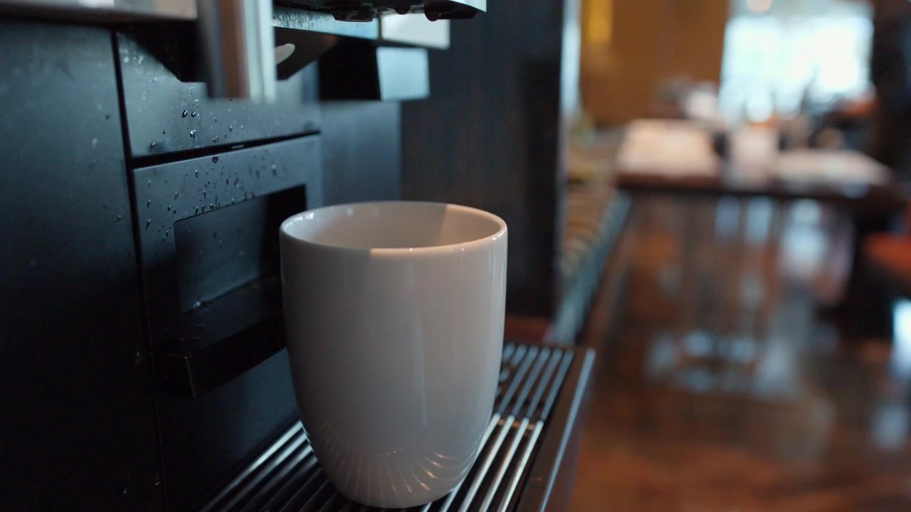 Primo piano fisso di una macchina da caffè espresso nera che versa caffè in una tazza bianca.