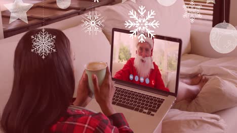 Animation-of-snow-falling-over-mixed-race-woman-on-laptop-video-call-with-santa-at-christmas