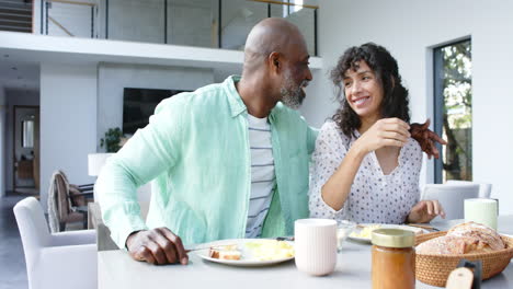 Feliz-Pareja-Birracial-Desayunando-Huevos-Revueltos-Y-Hablando-En-La-Cocina,-Cámara-Lenta