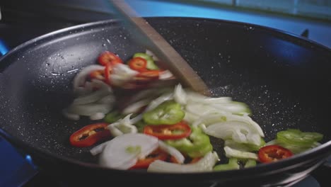 a close up looking into a skillet of oiled sliced onions and peppers and then stirred with a wooden spatula