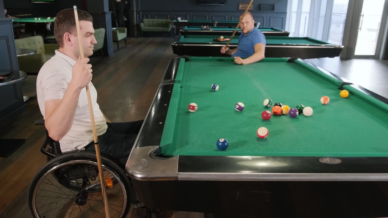 Adult men with disabilities in a wheelchair play billiards in the club