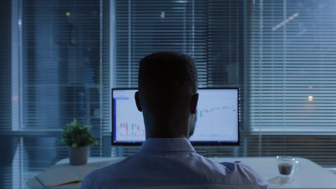 comerciante afroamericano trabajando en la computadora con gráfico de mercado de valores en la oficina oscura